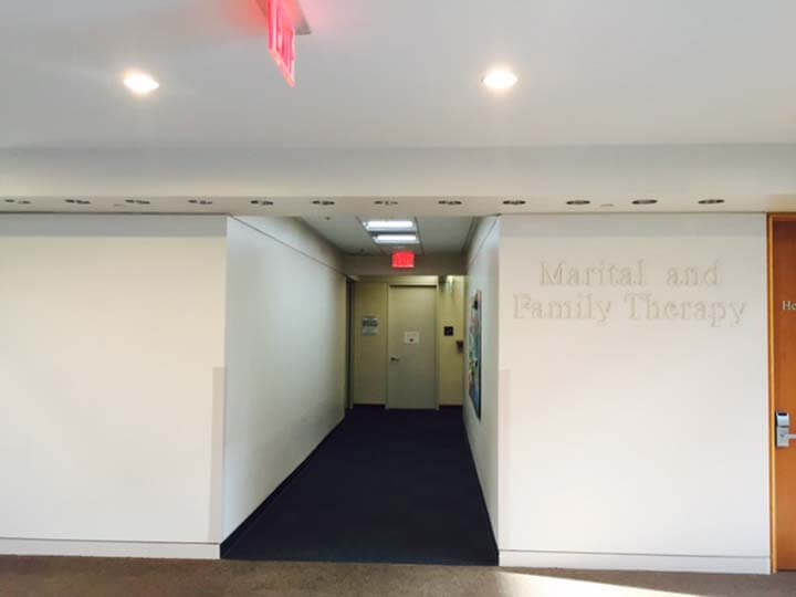 A hallway with white walls and black carpet.