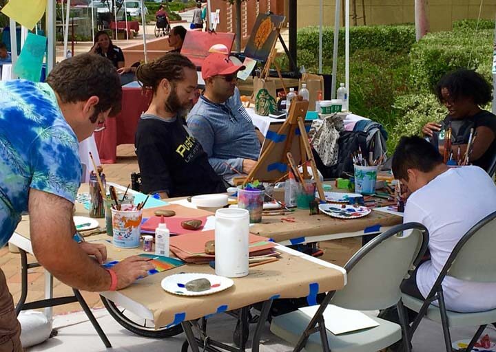 A group of people sitting at tables with paint brushes.