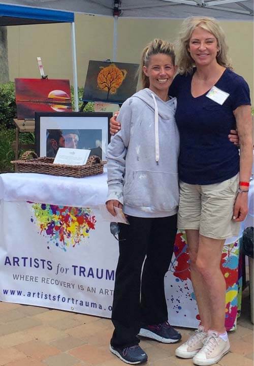 Two women standing next to a table with paintings on it.